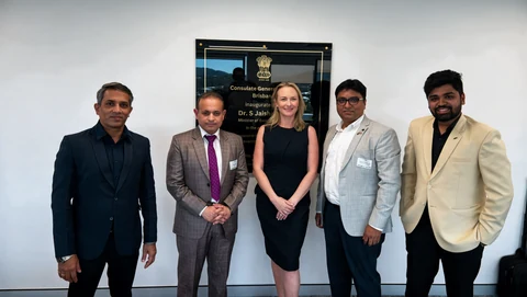 Five people standing together in a meeting venue in front of a wall plaque.