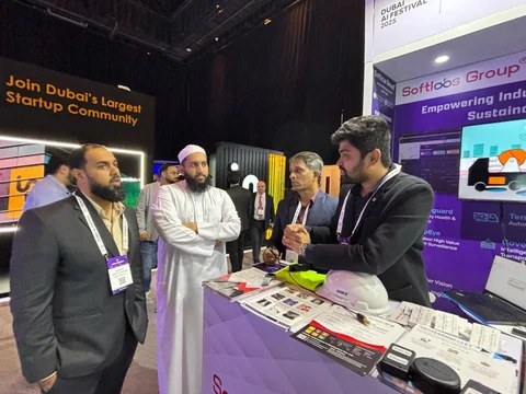 People in conversation at a Softlabs exhibition stand, with a demo table in front.