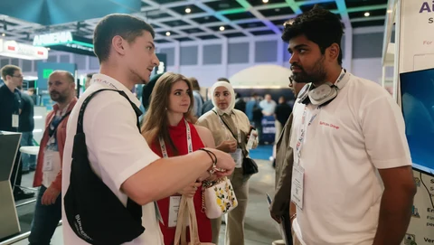 A Softlabs representative talking with visitors in a busy exhibition hall.