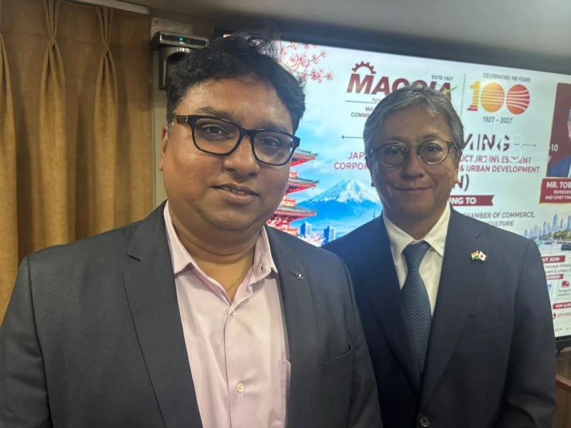Two participants at the India–Japan business interaction, with MACCIA event signage behind them.